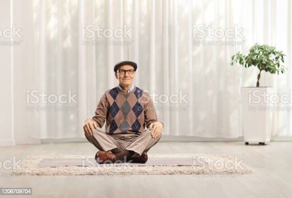 Senior man sitting on the floor and meditating at home Man sitting cross legged