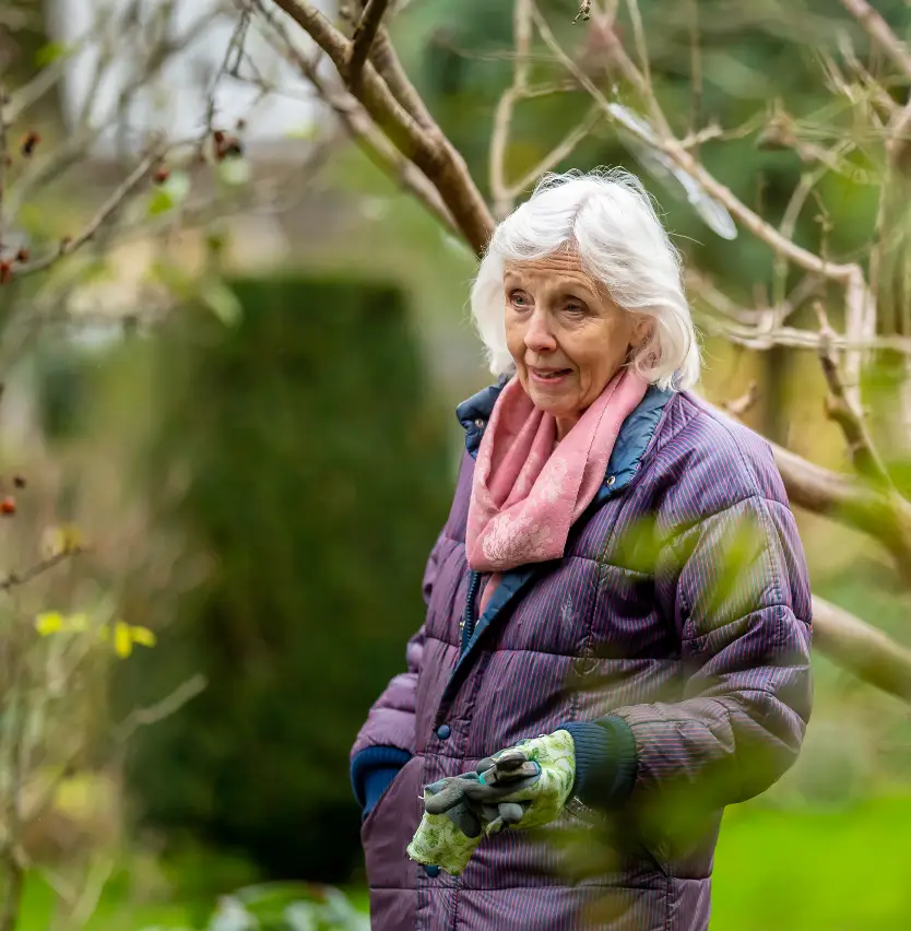 An older woman standing by a tree